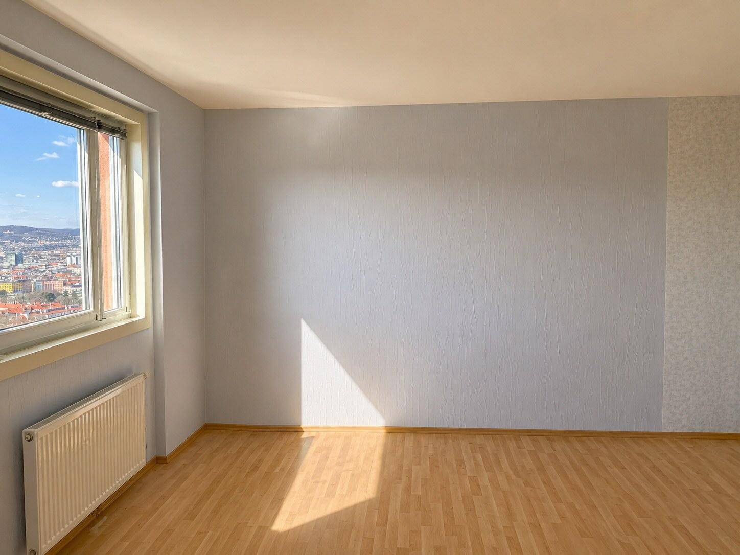 Helles Zimmer mit Parkettboden und einem Fenster, das einen Blick auf die Stadt bietet.