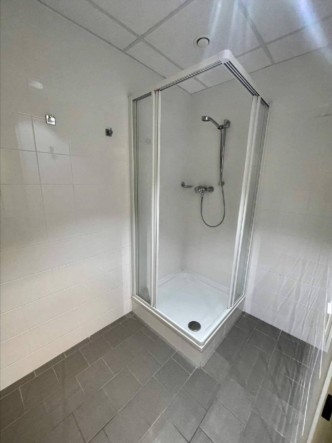 Einfaches Badezimmer mit einer Duschkabine, weißen Wandfliesen und grauen Bodenfliesen.