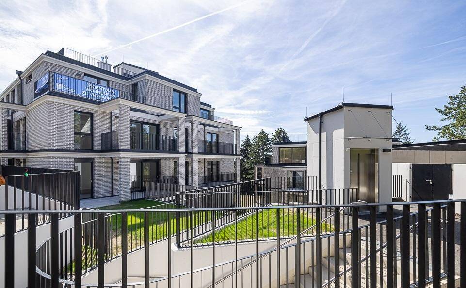 Moderne Wohnanlage mit mehreren Gebäuden, Balkonen, Tiefgaragenzufahrt und sichtbarem Aufzug.