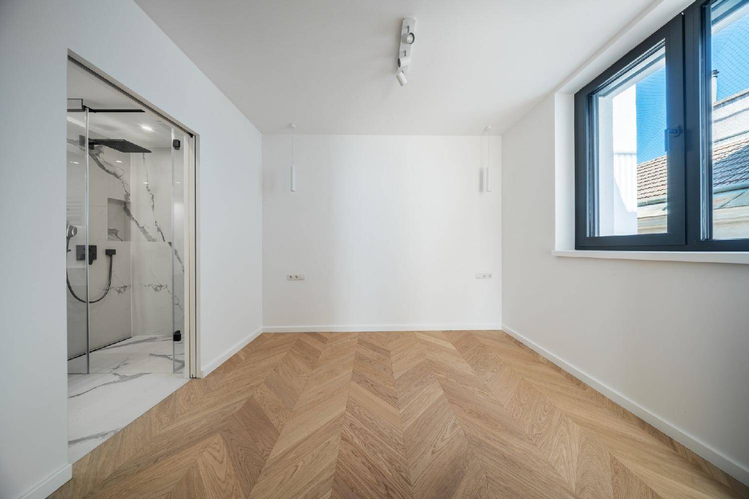 Schlafzimmer mit Fischgrätparkett und direktem Zugang zu einem modernen Bad mit begehbarer Dusche.