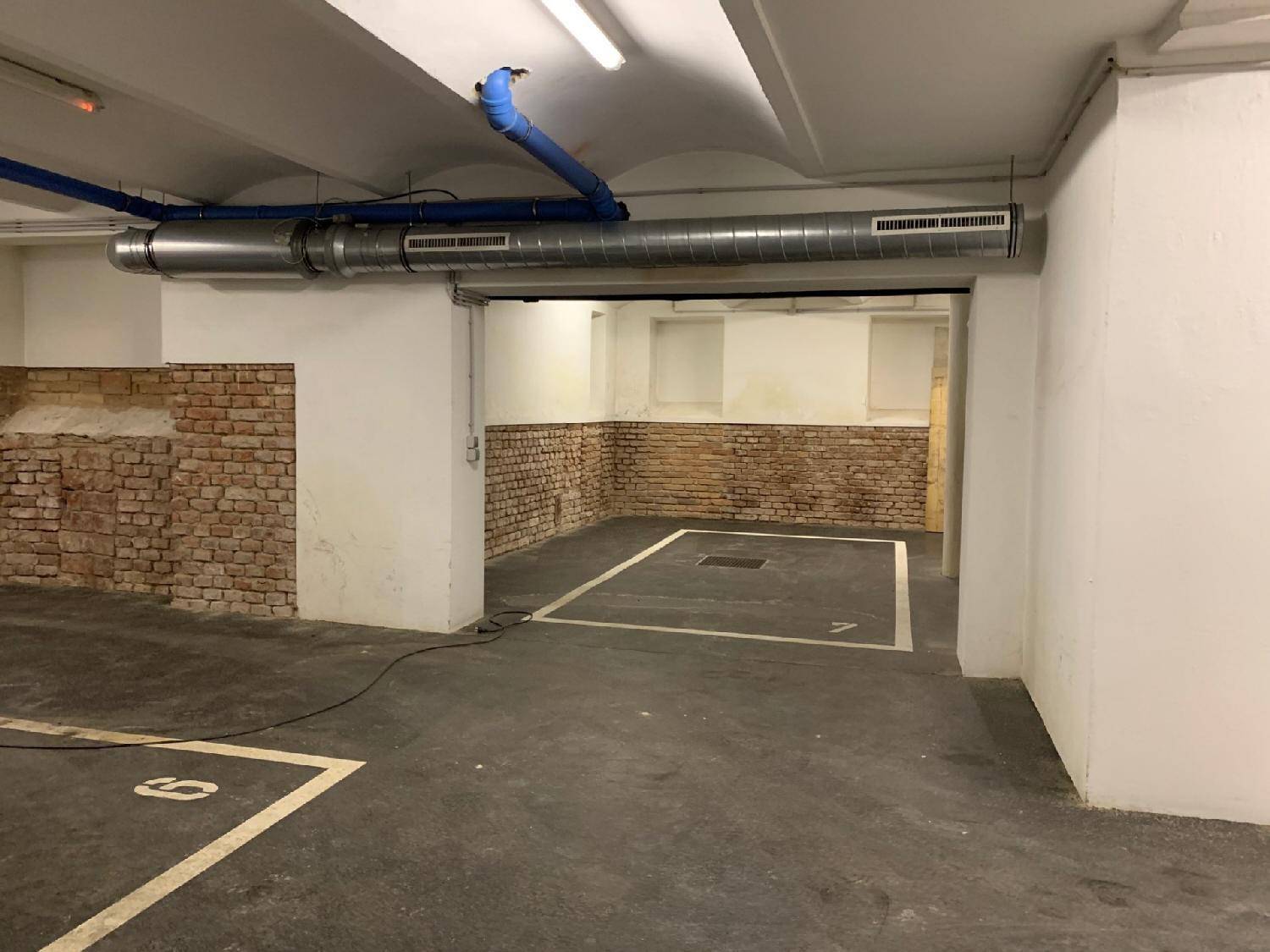 Tiefgarage mit markierten Stellplätzen, unverputzten Ziegelwänden und sichtbaren Installationen an der Decke.