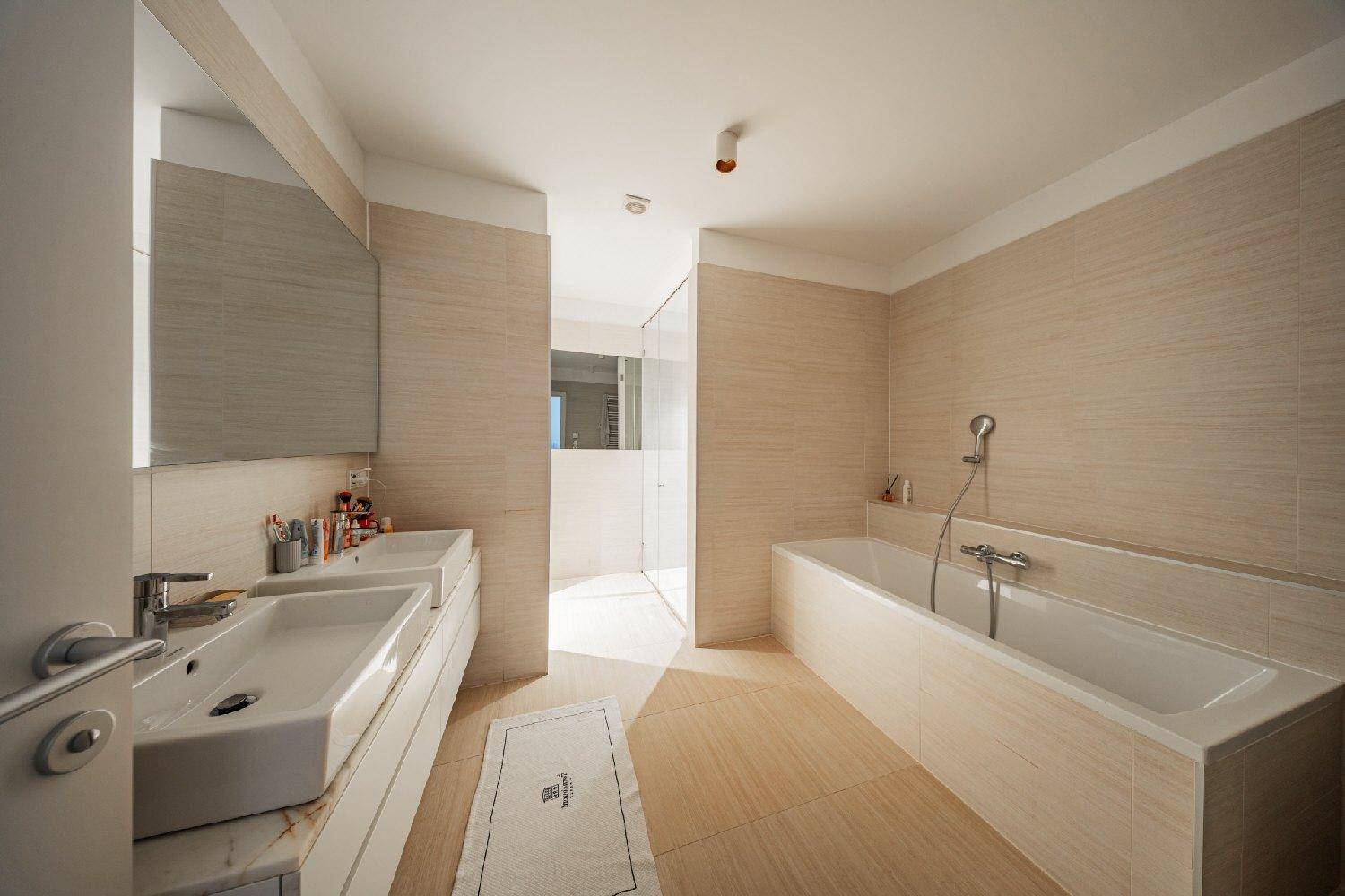 Helles Badezimmer mit Doppelwaschbecken, Badewanne und ebenerdiger Dusche.