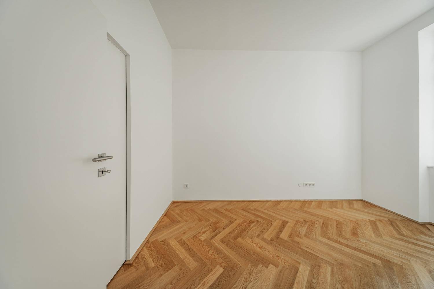 Heller Raum mit neuem Fischgrätparkett und einer modernen weißen Tür, bereit zur Einrichtung.