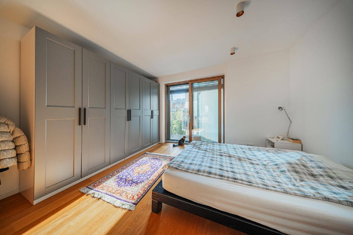 Schlafzimmer mit Holzboden, großem Kleiderschrank und Zugang zu einem Balkon.