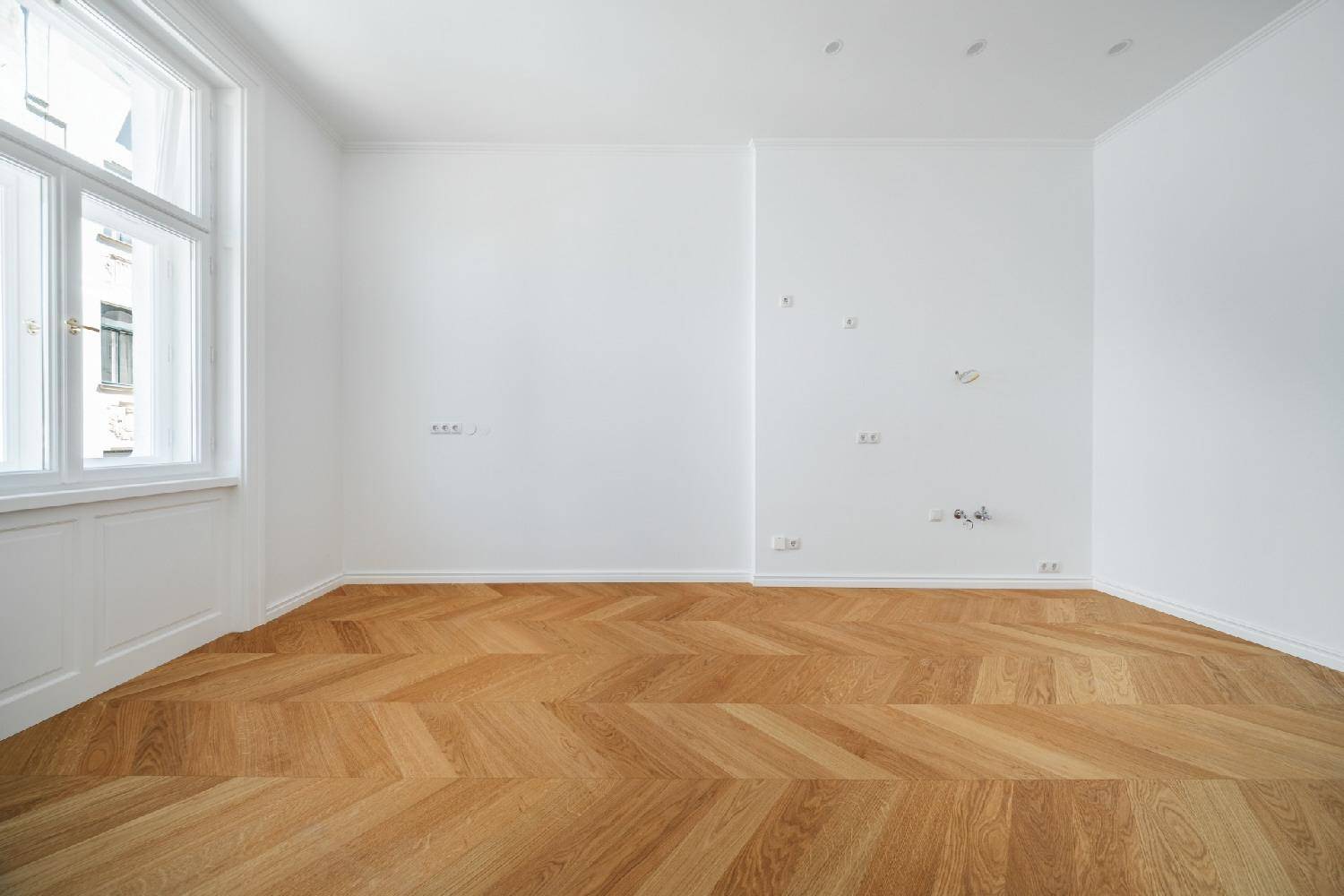 Geräumiges, helles Zimmer mit Fischgrätparkett und großen Fenstern, ideal für vielfältige Nutzung.
