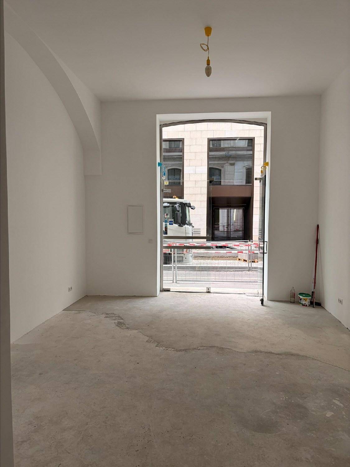 Heller, leerer Raum mit großen Glasfronten zur Straße und Blick auf die städtische Umgebung.