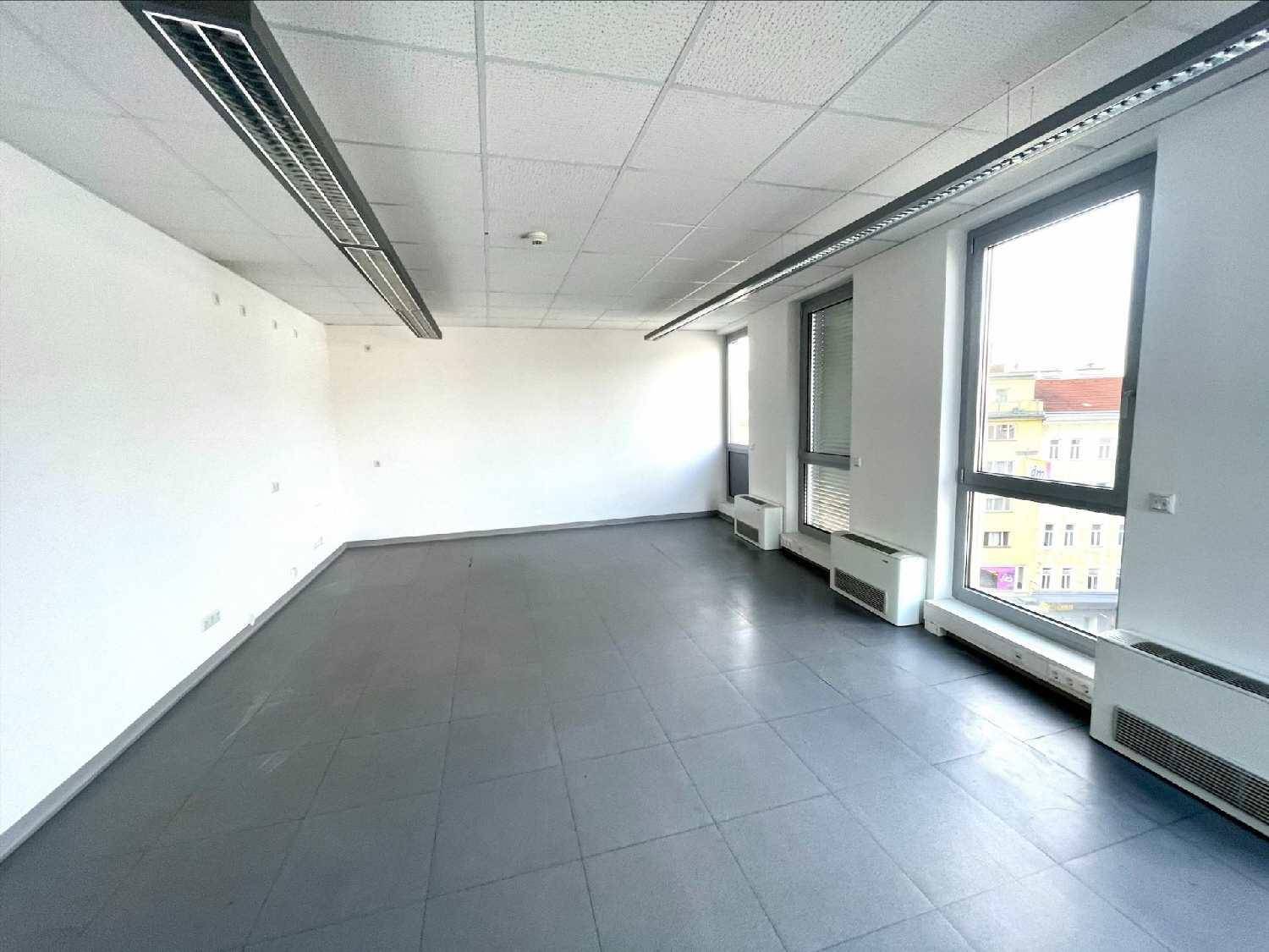 Geräumiger, leerer Büroraum mit großen Fenstern, die viel Tageslicht hereinlassen und grauen Fliesen.