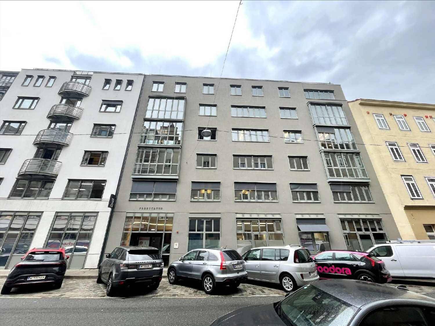 Mehrstöckiges Gebäude mit moderner Fassade, großen Fenstern und parkenden Autos davor.