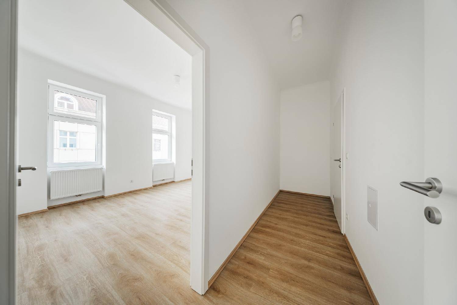 Heller Flur mit Laminatboden, der in einen weiteren Raum mit großen Fenstern führt.