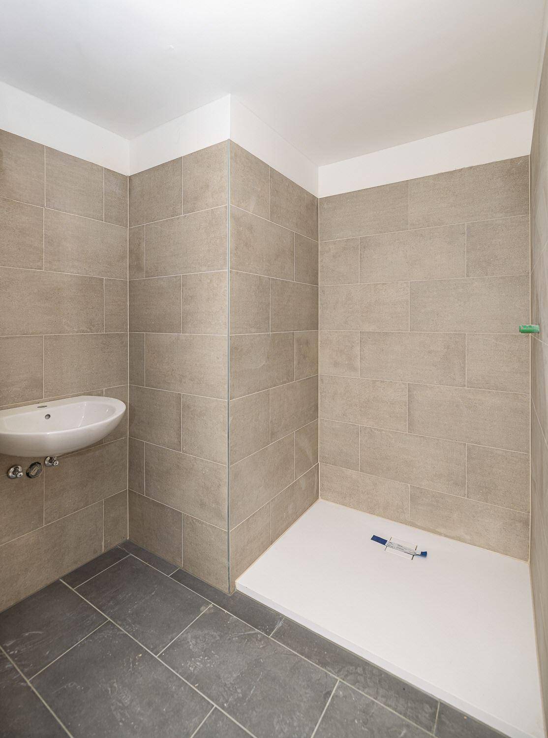Unfertiges Badezimmer mit beigefarbenen Wandfliesen, dunklem Boden und einer ebenerdigen Dusche.