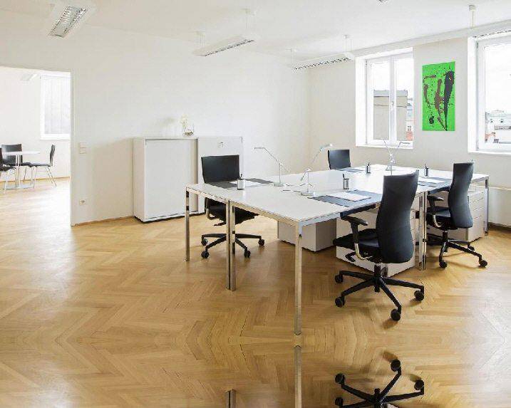 Helles und offenes Büro mit mehreren Arbeitsplätzen, weißen Schränken und großen Fenstern.