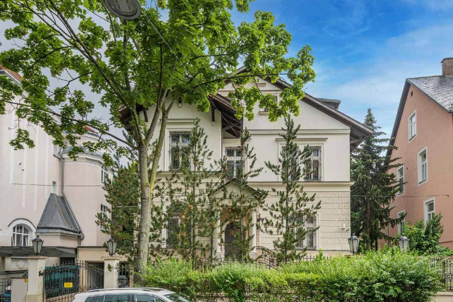 Repräsentative Fassade einer Stadtvilla, umgeben von altem Baumbestand und gepflegter Hecke.