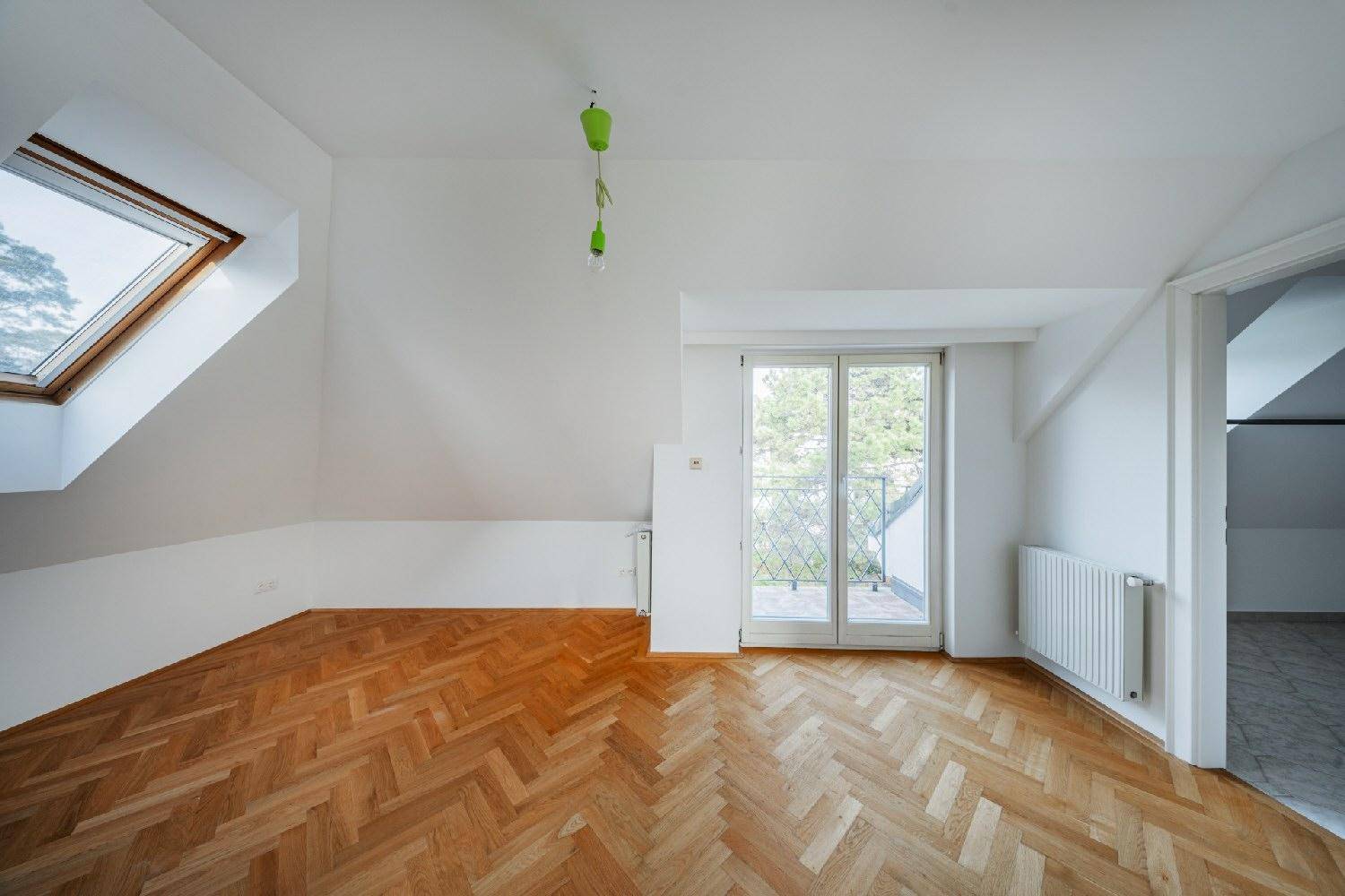 Helles Dachzimmer mit schrägen Wänden, Dachfenster und Zugang zu einem kleinen Balkon.