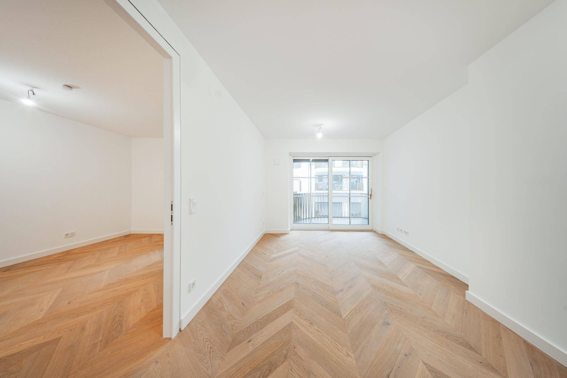 Geräumiges, helles Wohnzimmer mit Fischgrätparkett und Schiebetür zum Balkon.