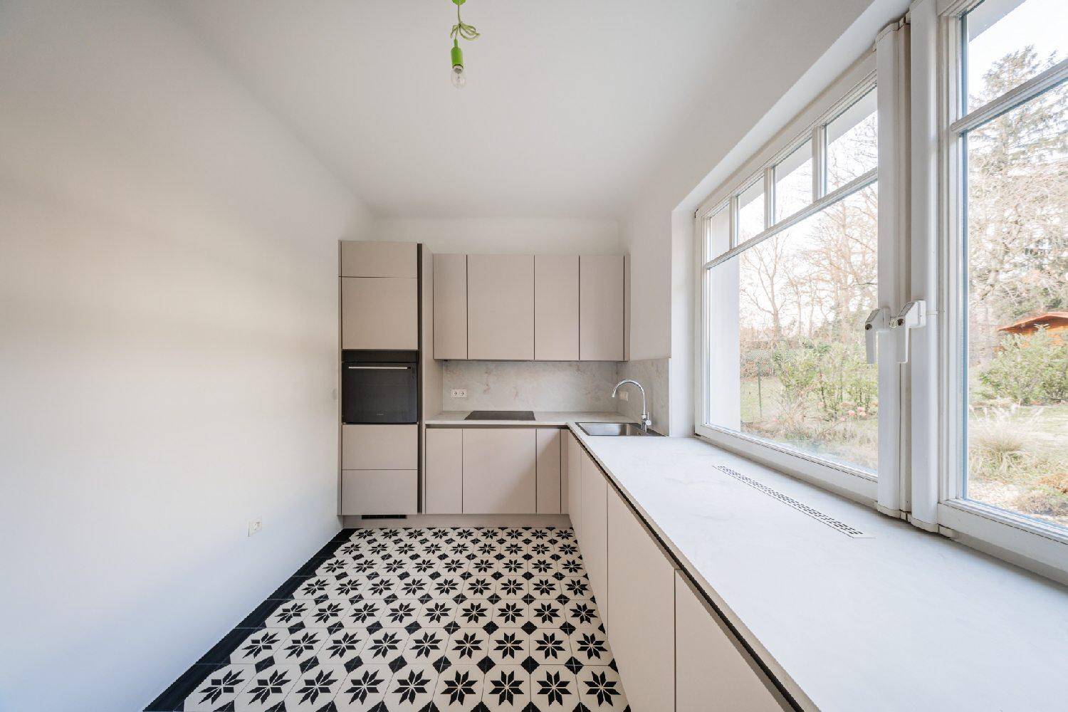 Moderne Einbauküche mit hellen Schränken, integriertem Backofen und großem Fenster mit Gartenblick.