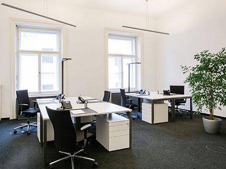 Helles Büro mit mehreren Arbeitsplätzen, großen Fenstern und einer Zimmerpflanze.