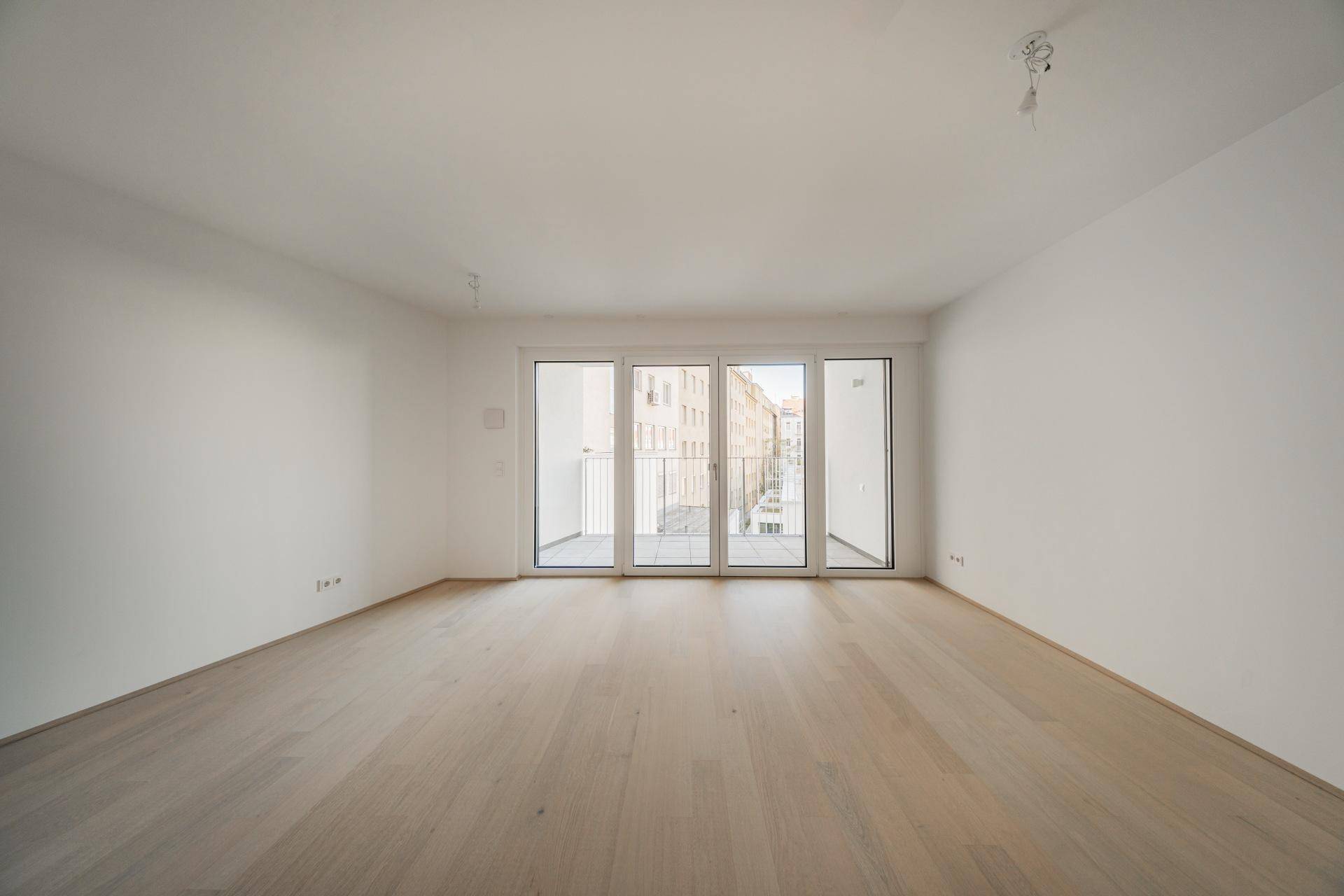 Geräumiges, unmöbliertes Zimmer mit hellem Parkett und Zugang zu einem französischen Balkon.