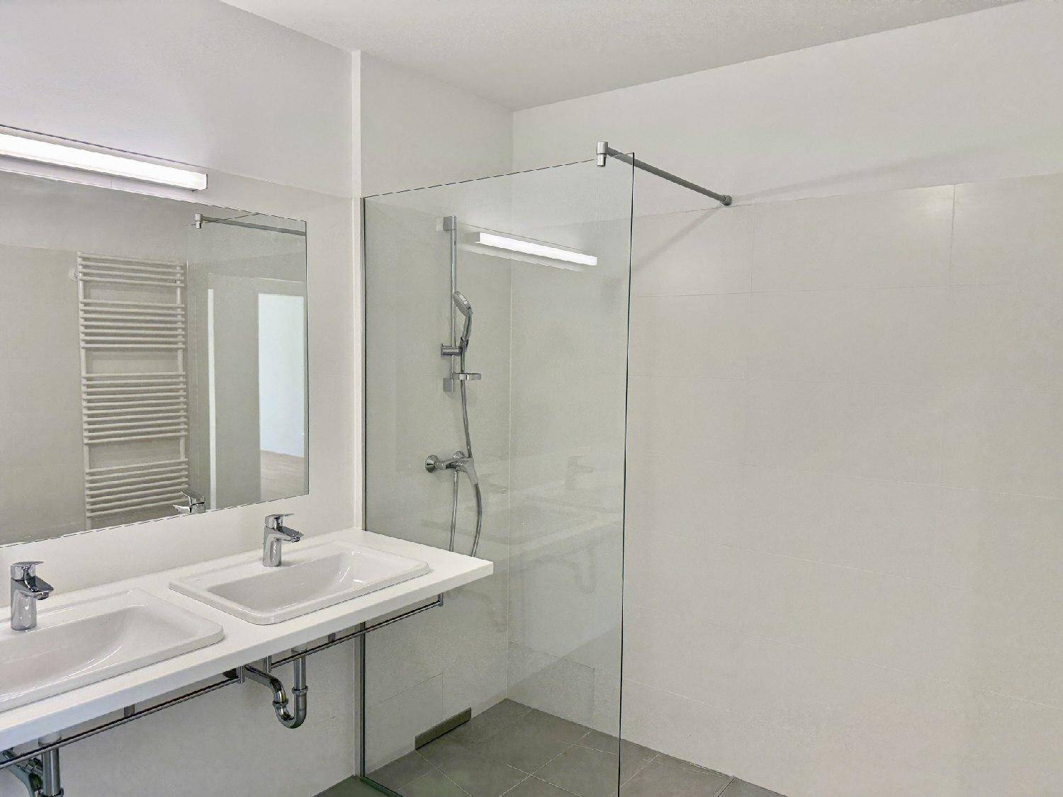 Modernes Badezimmer mit Doppelwaschbecken, großer begehbarer Dusche und beheiztem Handtuchhalter.