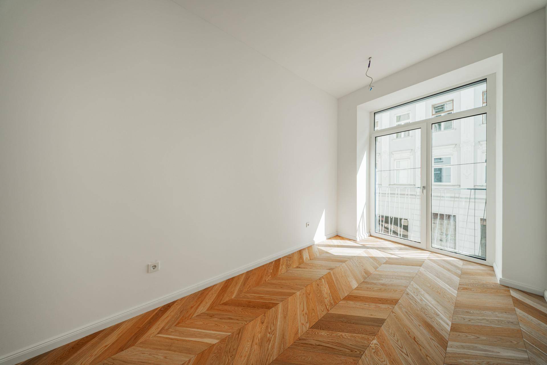Geräumiges Zimmer mit hellem Fischgrätparkett und großem Fenster, das für eine freundliche Atmosphäre sorgt.