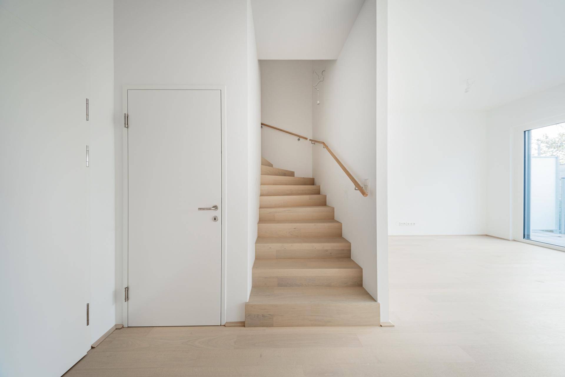 Heller Eingangsbereich mit Holztreppe und Zugang zu den oberen Etagen.