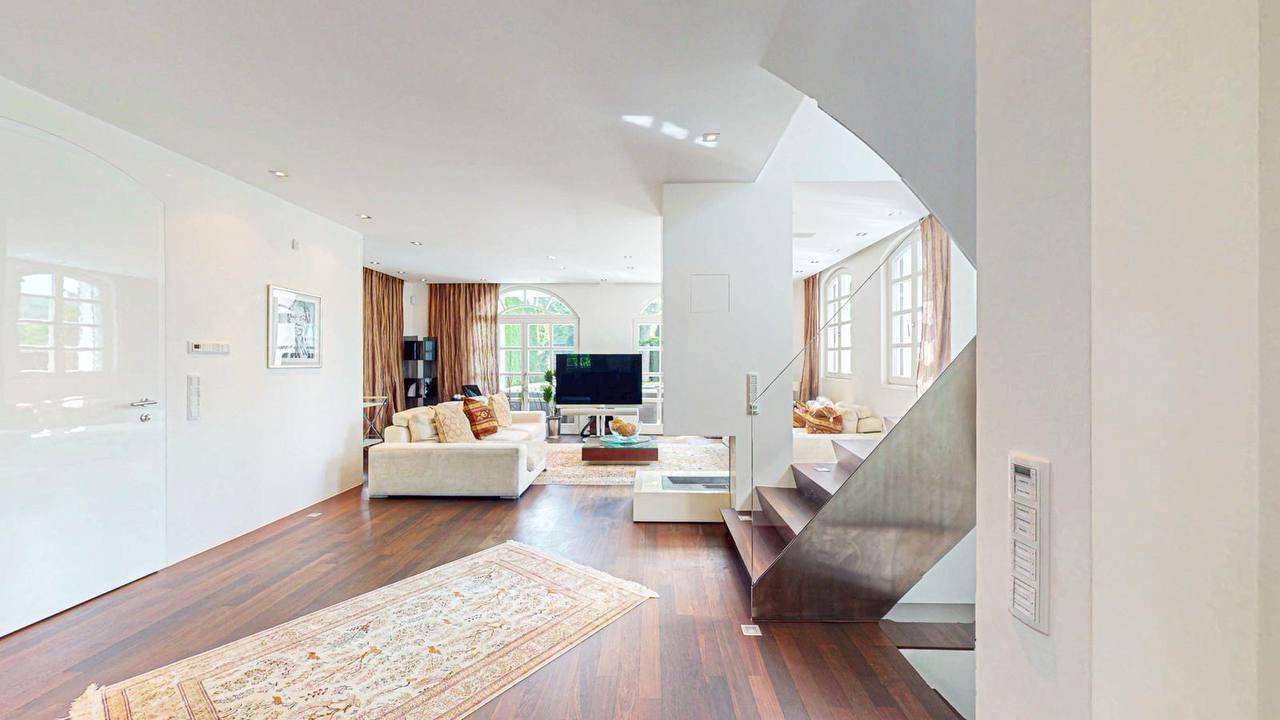 Geräumiges Wohnzimmer mit dunklem Parkettboden und Zugang zur offenen Treppe.