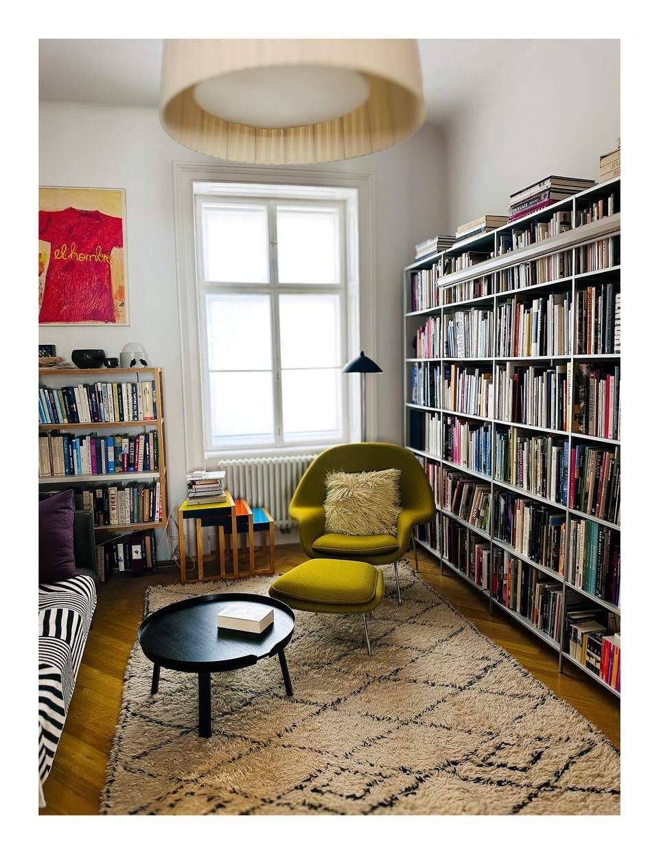 Helle Bibliothek mit umfangreichen Bücherregalen, einem gelben Sessel und Teppich.
