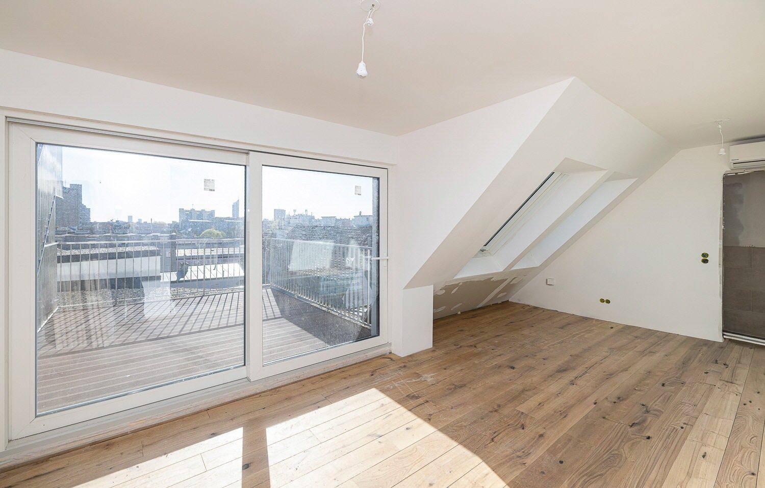 Lichtdurchfluteter Raum im Dachgeschoss mit Zugang zu einem Balkon und Blick auf die Stadt.