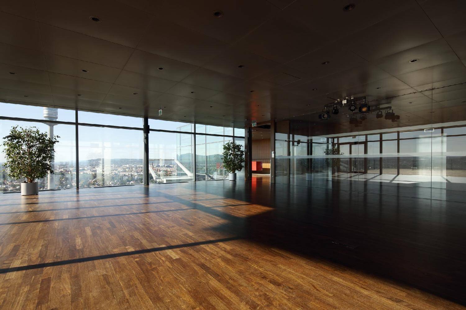 Geräumiger Saal mit Holzboden, großen Fenstern und beeindruckendem Stadtpanorama.
