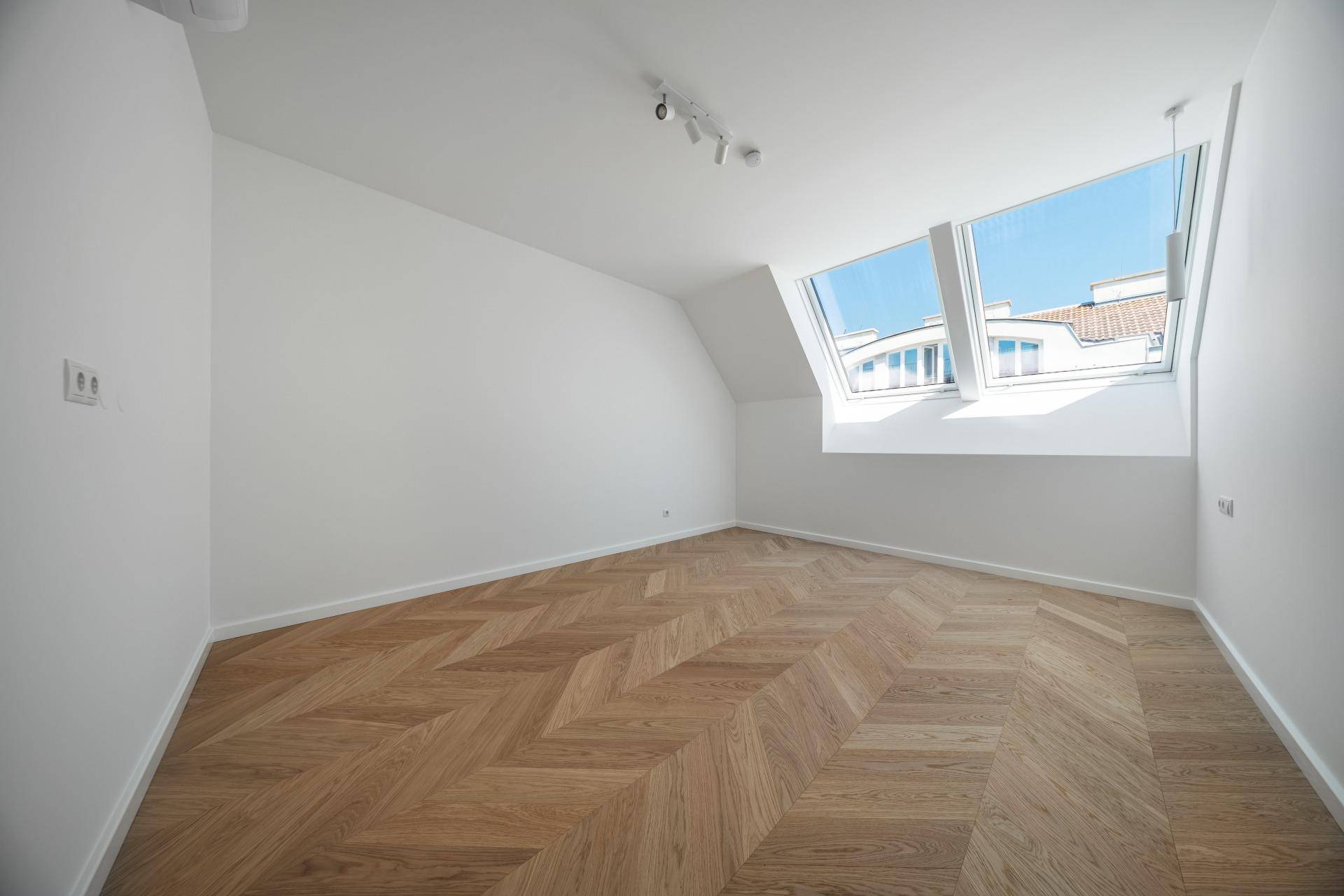 Ruhiges Schlafzimmer mit Fischgrätparkett, weißen Wänden und einem Dachfenster, das viel Licht spendet.