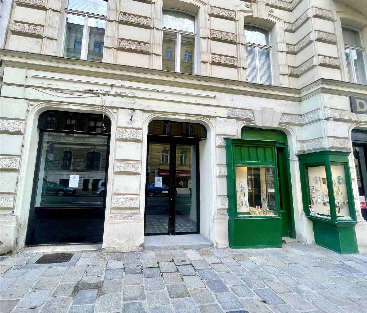 Historische Gebäudefassade mit großen Schaufenstern und einem grünen Ladeneingang an einer Kopfsteinpflasterstraße.
