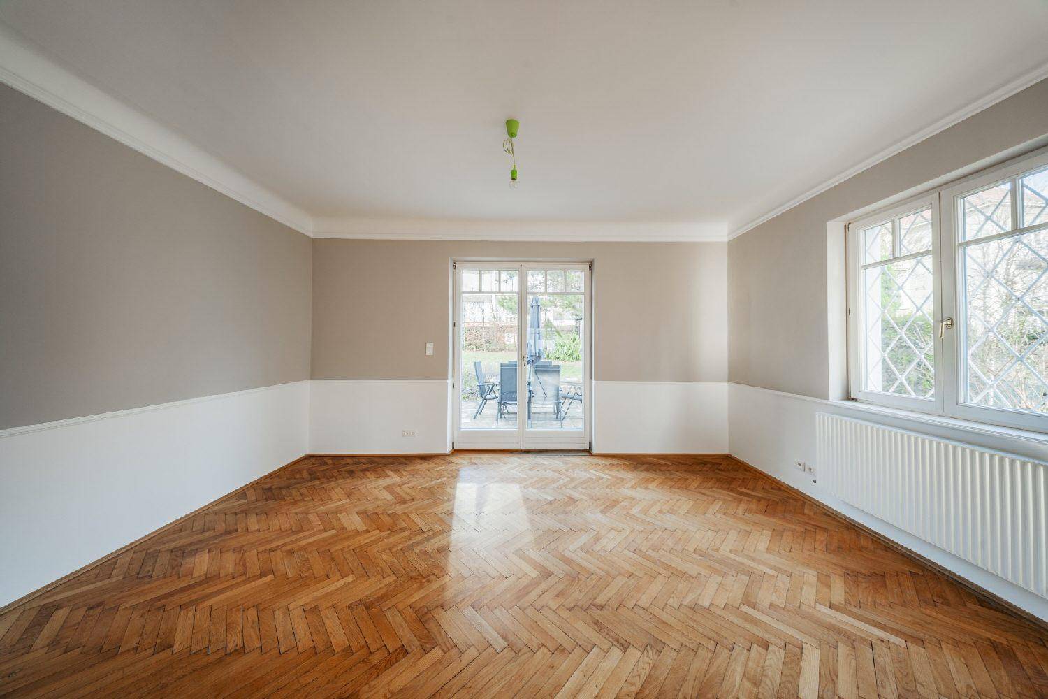 Geräumiges Wohnzimmer mit Fischgrätparkett und großen Fenstertüren zur Außenterrasse und Garten.