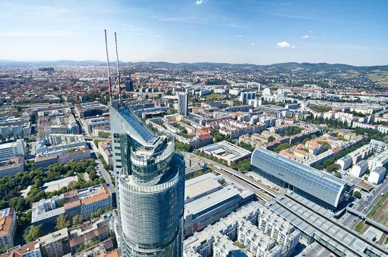 Luftaufnahme der Stadt mit einem markanten Hochhaus und umliegenden Gebäuden unter blauem Himmel.