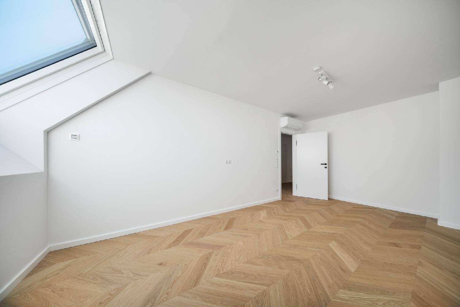 Helles Schlafzimmer mit Fischgrätparkett, Dachfenster und integrierter Klimaanlage.