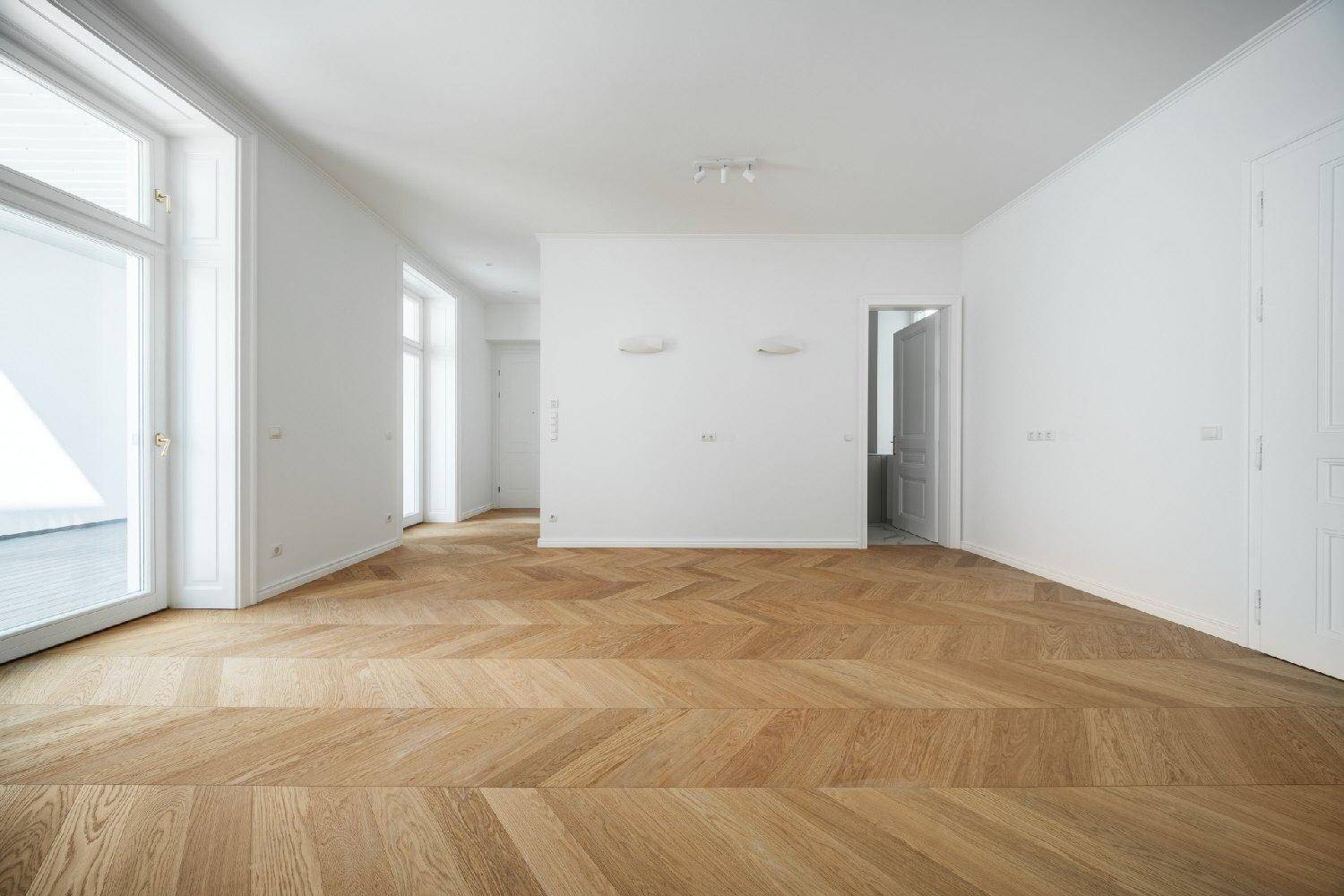 Weitläufiger, heller Raum mit elegantem Fischgrätparkett und mehreren Fenstern.