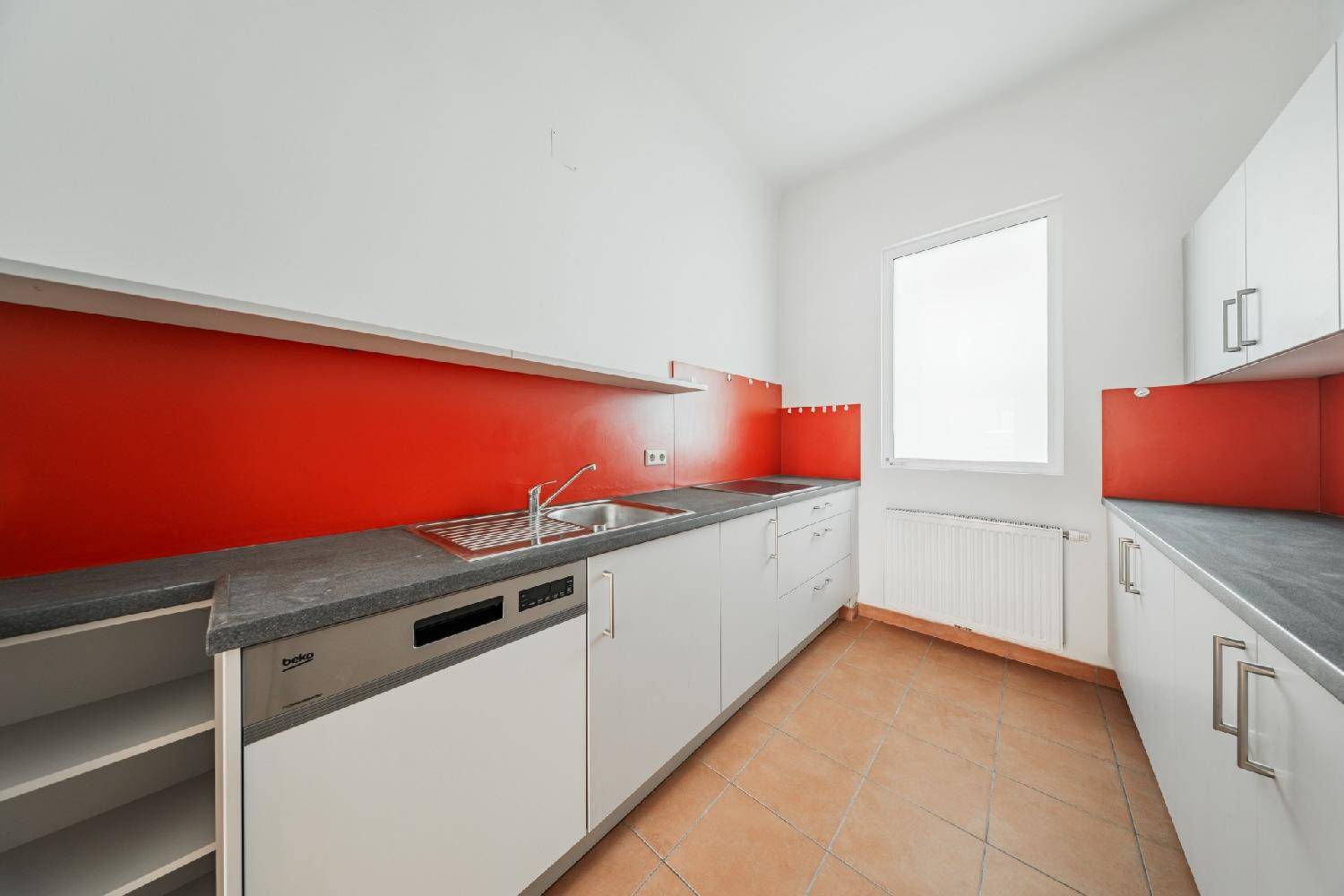 Funktionale Küche mit grauen Unterschränken, roter Rückwand und Spülmaschine, hell und praktisch.