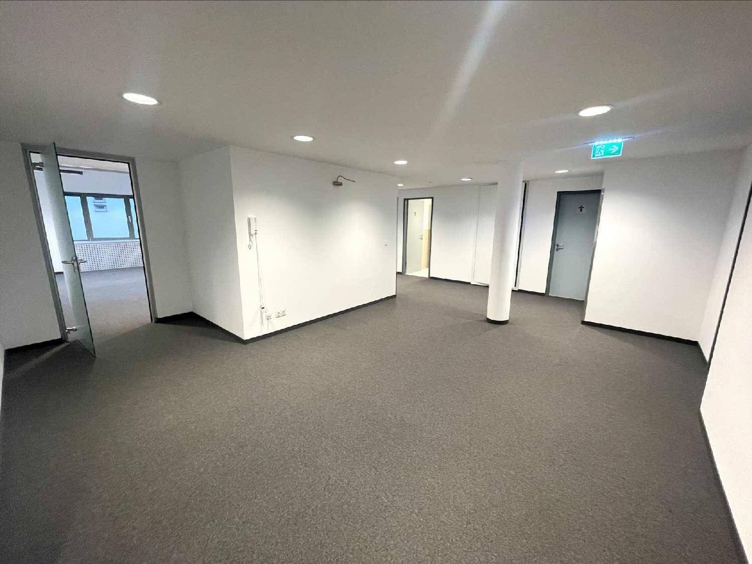Heller Bürobereich mit Teppichboden, weißen Wänden und mehreren Türen zu angrenzenden Räumen.
