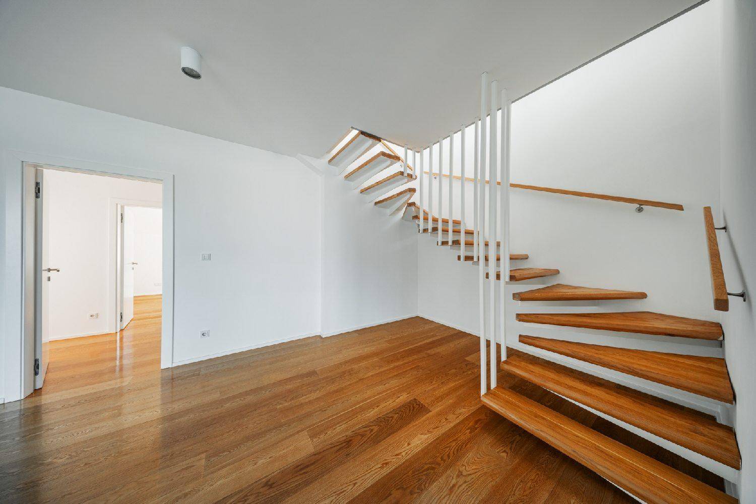 Moderne Holztreppe mit weißem Geländer, die die verschiedenen Ebenen des Wohnraums verbindet.