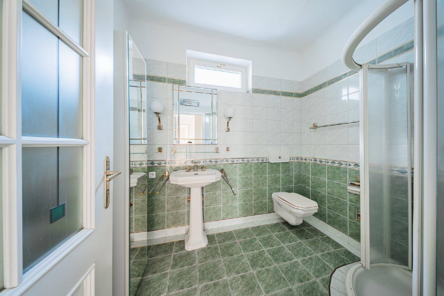 Badezimmer mit grünen Fliesen, Standwaschbecken, Toilette und einer Duschkabine im Eck.