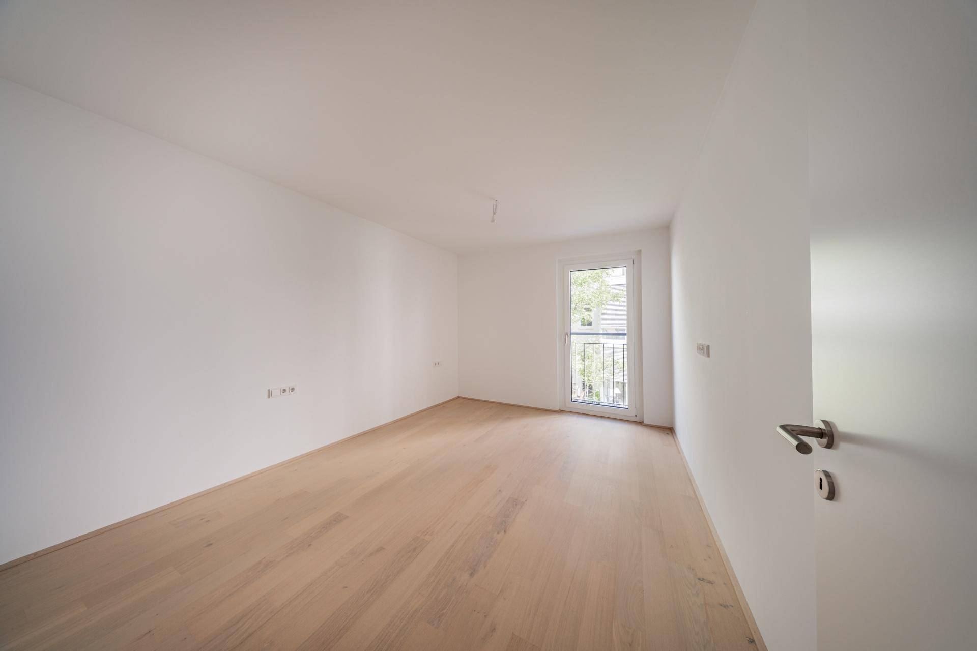 Leeres Schlafzimmer mit hellem Holzfußboden und einem französischen Balkon.