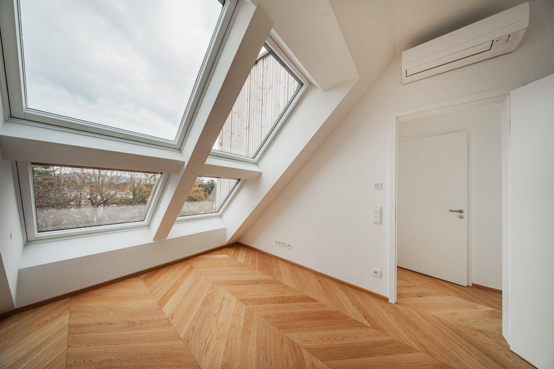 Helles Zimmer im Dachgeschoss mit schrägen Wänden, Dachfenstern und Klimaanlage, bereit zum Einzug.