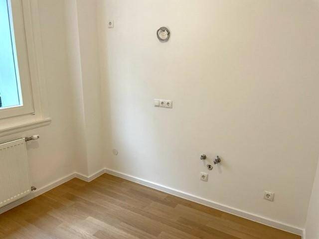 Kleiner Raum mit Fenster, Holzfußboden und Anschlüssen für eine zukünftige Küche oder Waschküche.