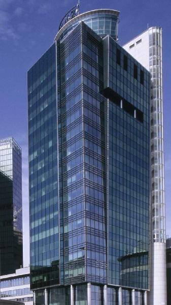 Zeitgenössisches Hochhaus mit blauer Glasfassade und markanter Dachkonstruktion in urbaner Umgebung.