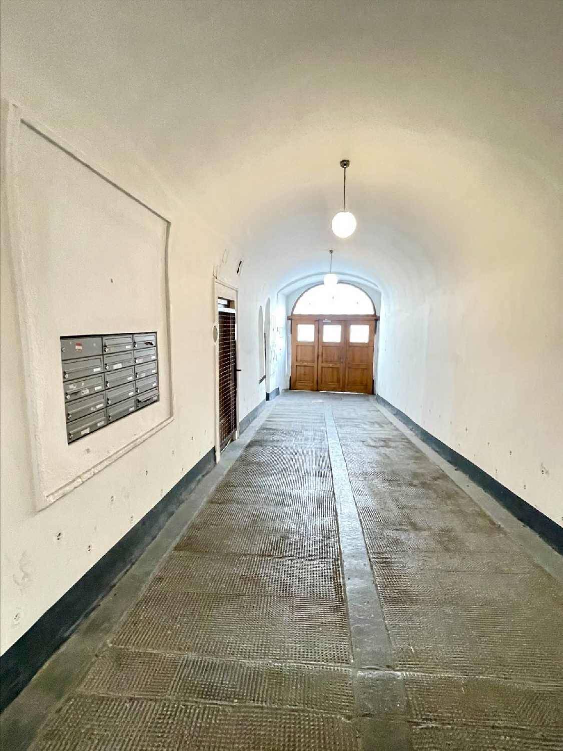 Gewölbter Eingangsbereich mit dunklem Boden und Briefkästen an der Wand, der zum Gebäude führt.