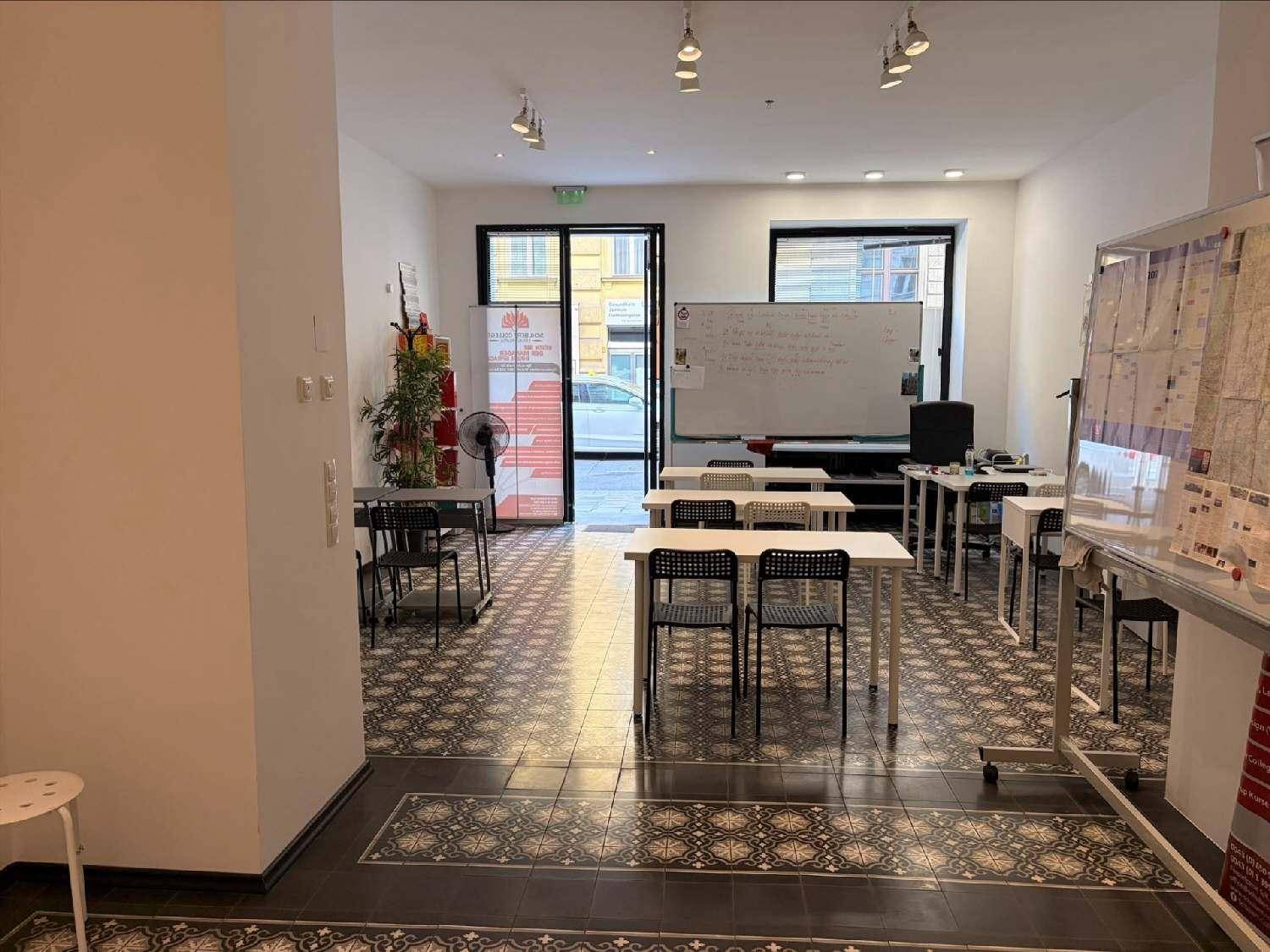 Geräumiger Klassenraum mit vielen Tischen und Stühlen, einer Whiteboard-Tafel und Blick zur Straße.