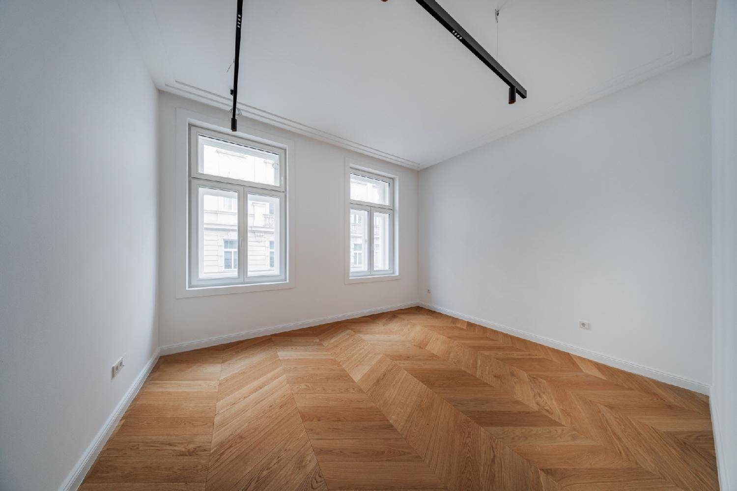 Helles Zimmer mit Fischgrätparkett und zwei Fenstern, ideal als Schlaf- oder Arbeitszimmer.