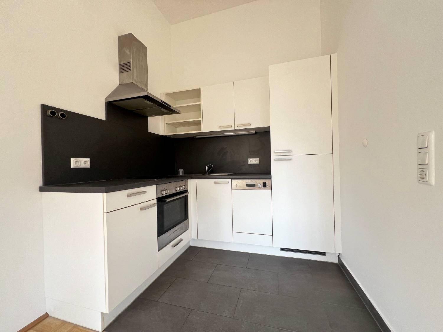 Moderne Einbauküche mit weißen Schränken, dunkler Arbeitsplatte und integrierten Geräten.