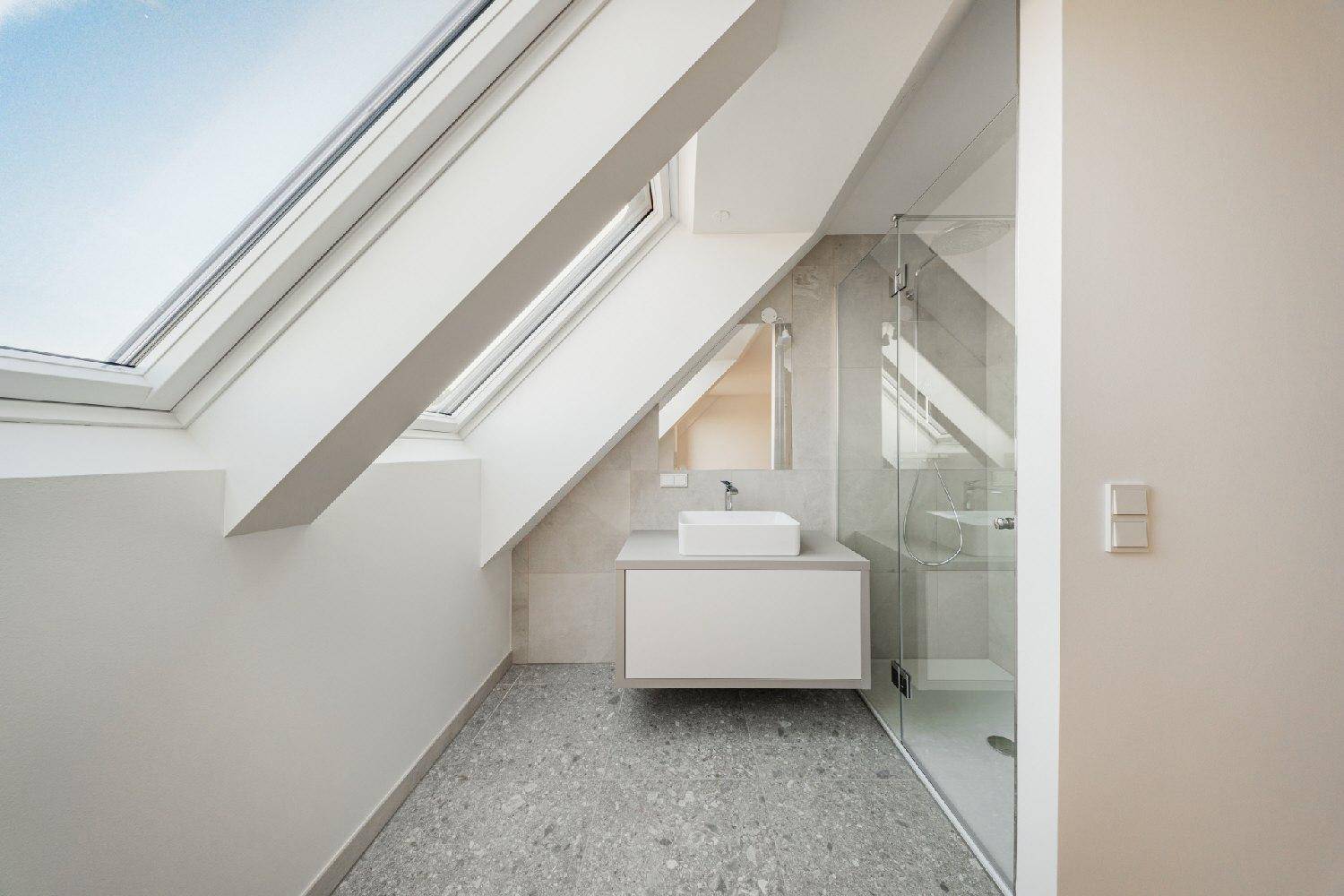 Modernes Badezimmer im Dachgeschoss mit Dusche, Waschtisch und Dachfenstern für natürliches Licht.