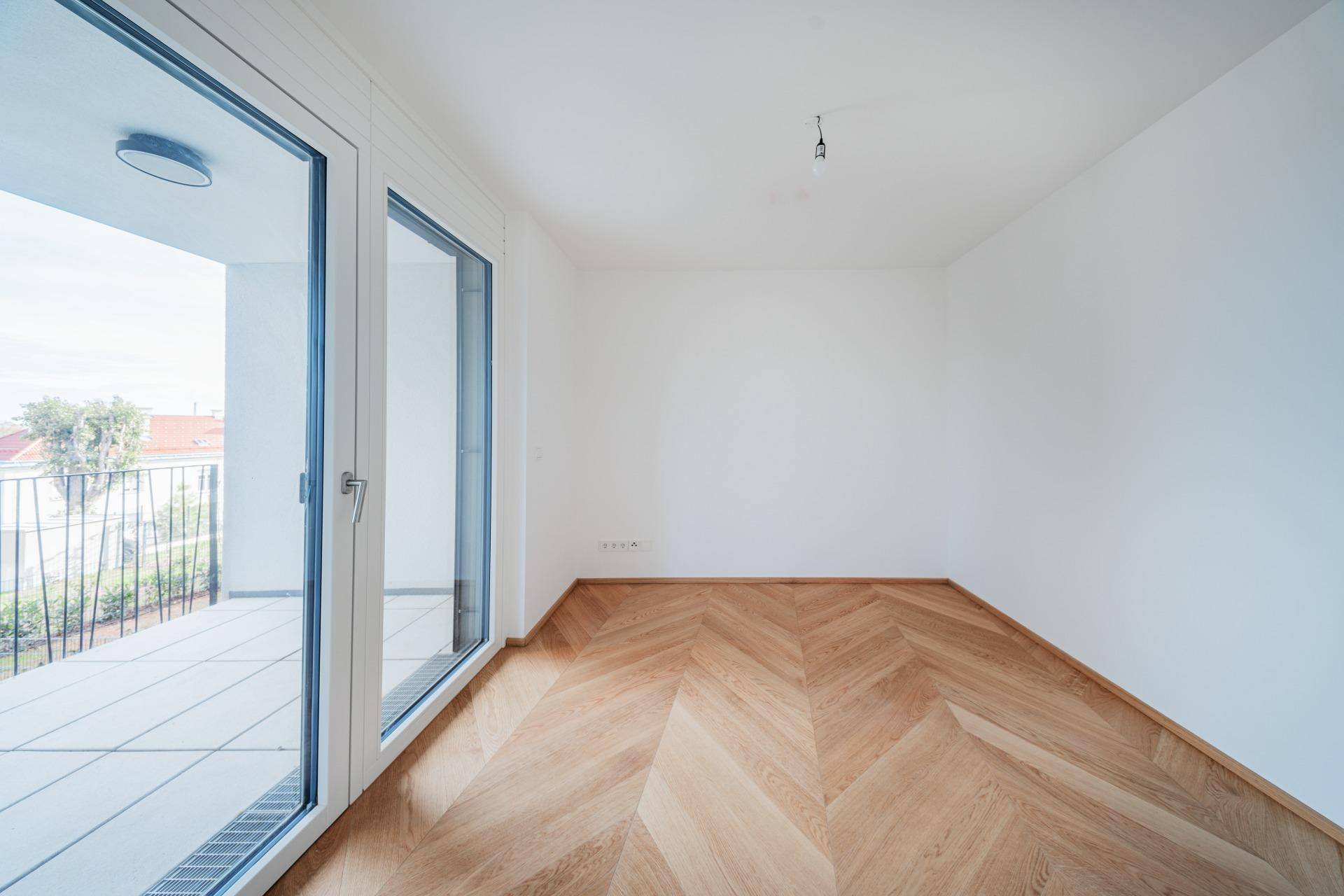 Freundliches Zimmer mit Fischgrätparkett und direktem Zugang zu einer gefliesten Terrasse.