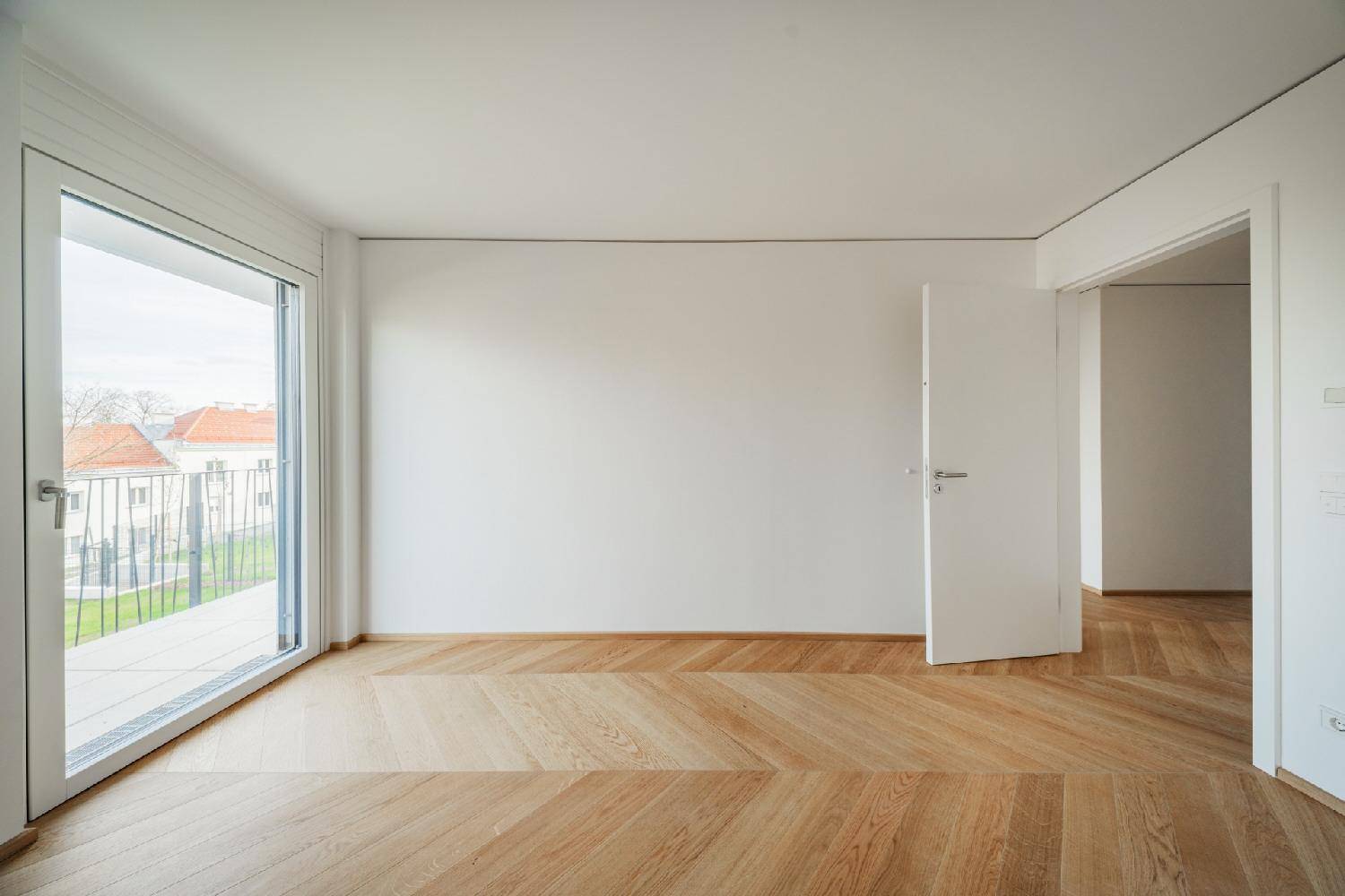Helles Zimmer mit Fischgrätparkett und Zugang zu einem französischen Balkon oder kleiner Terrasse.