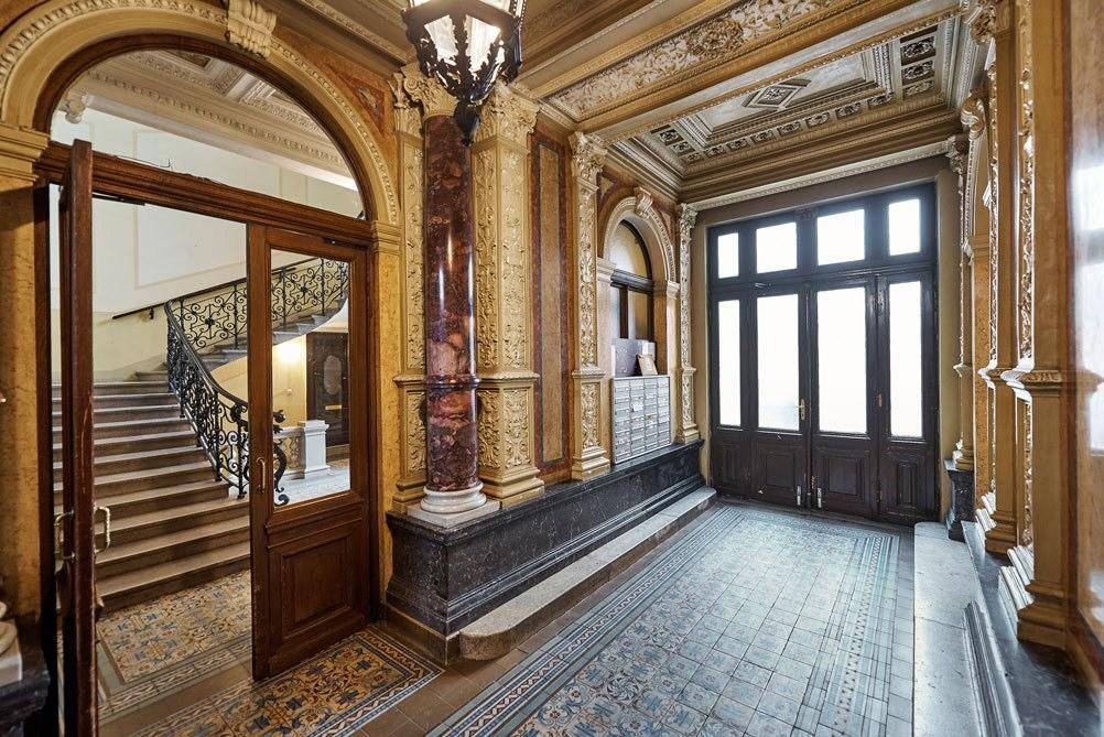 Prunkvoller Eingangsbereich mit Marmorverkleidung, Säulen und einem historischen Kronleuchter, der zum Treppenhaus führt.